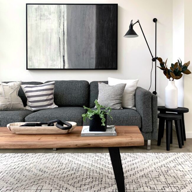 Trendy living room with wooden table, grey sofa and abstract painting